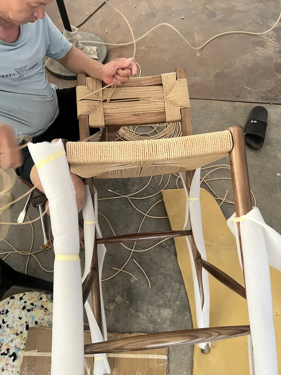 Hands pulling cord during the hand-weaving process of an Oslo stool